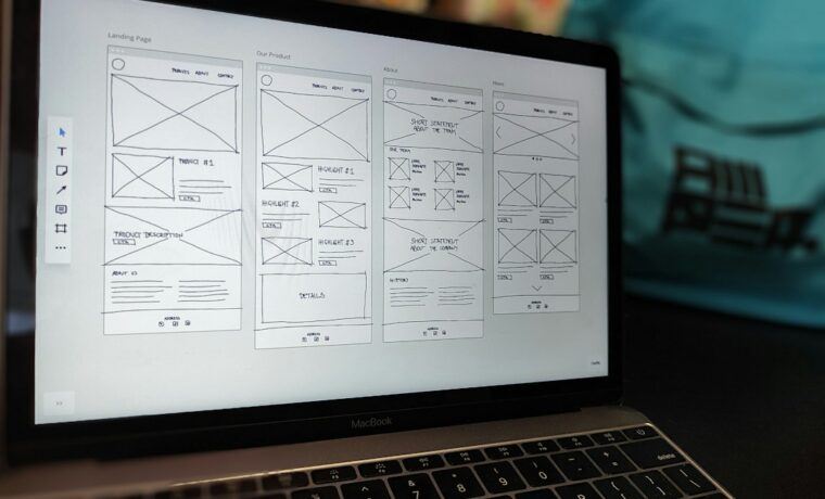 Designer sketching a landing page layout next to a laptop showing a website mock-up