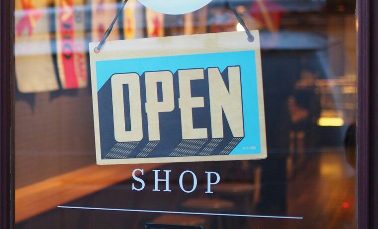 Small business owner standing at the entrance of a local shop with an open sign