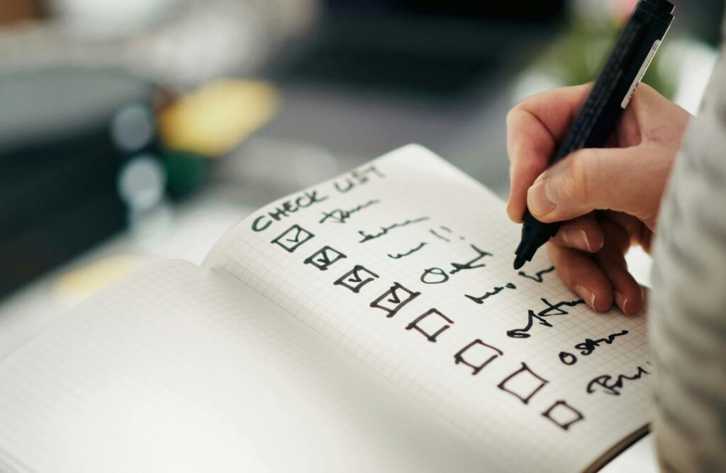 Person ticking off an on-page SEO checklist in a notebook beside a laptop