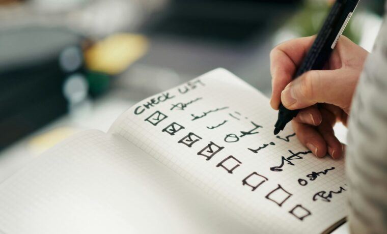 Person ticking off an on-page SEO checklist in a notebook beside a laptop